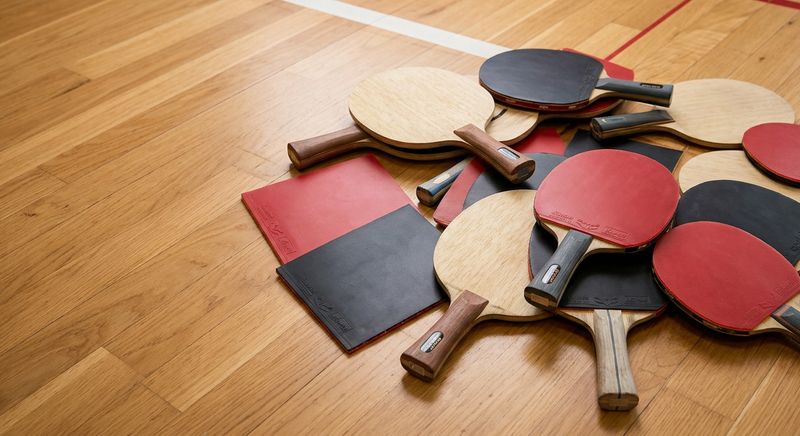 Haufen gebrauchter Tischtennisschläger und Beläge auf einem Holz-Hallenboden